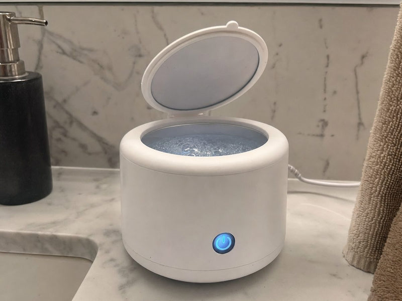 The Rinsa pod running on a marble bathroom counter, lid open and the water inside full of bubbles.